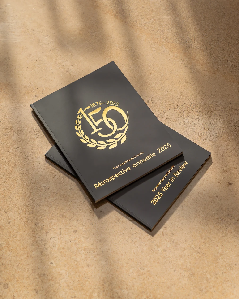 La version française de la Rétrospective annuelle 2025, avec la version anglaise en dessus. La couverture est bleu foncé avec le logo de l’anniversaire de la Cour en or.