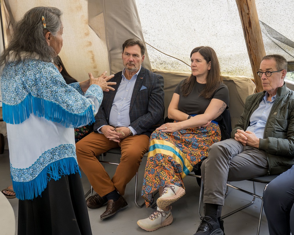 Chief Justice Wagner and Justices Kasirer and O’Bonsawin listening to an Elder speak in a tent.