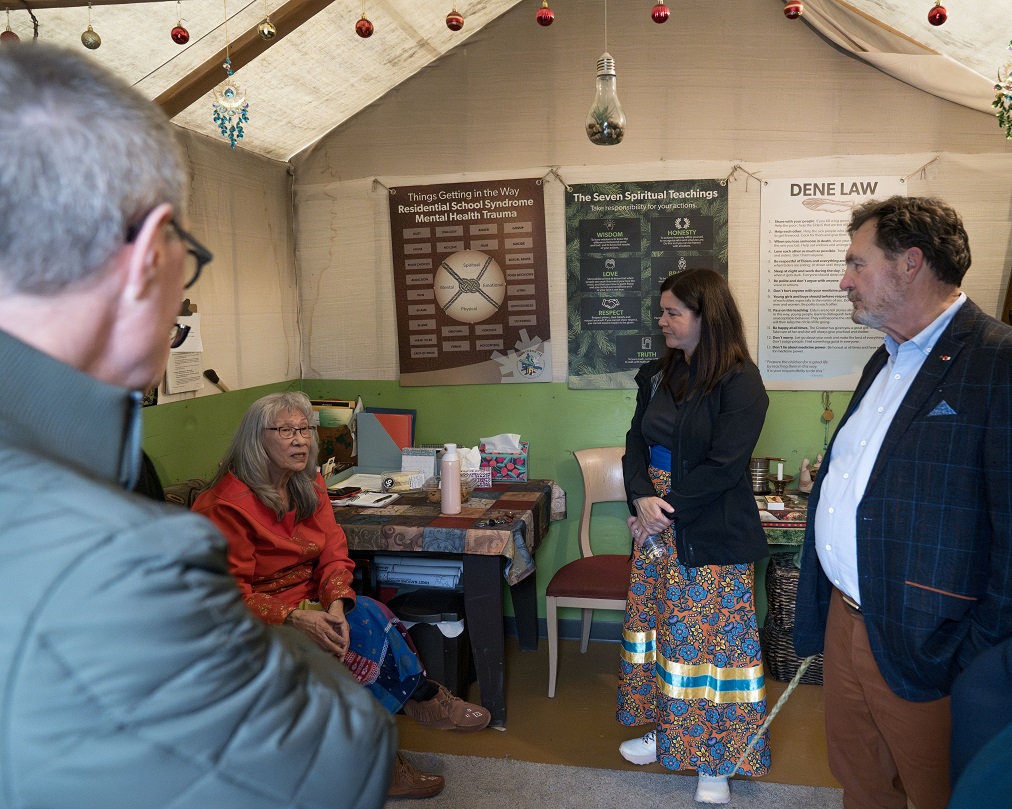 Chief Justice Wagner and Justices Kasirer and O’Bonsawin listening to an Elder speak in a tent.